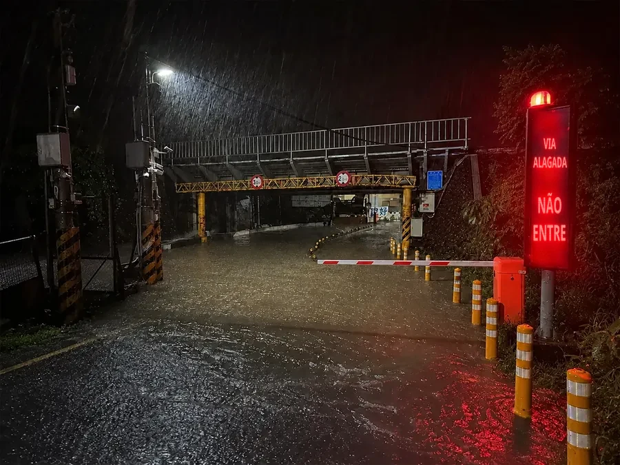 Aviso de fechamento por alagamento na entrada de uma passagem subterrânea, com sinalizadores e placas que impedem a entrada de veículos